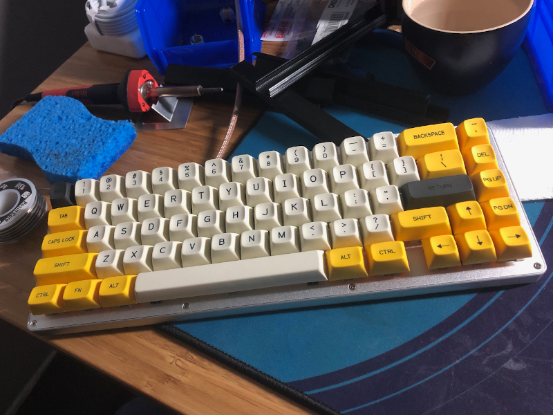 Completed White Fox keyboard sitting on a desk next to a soldering iron, blue sponge, and a coil of soldering wire